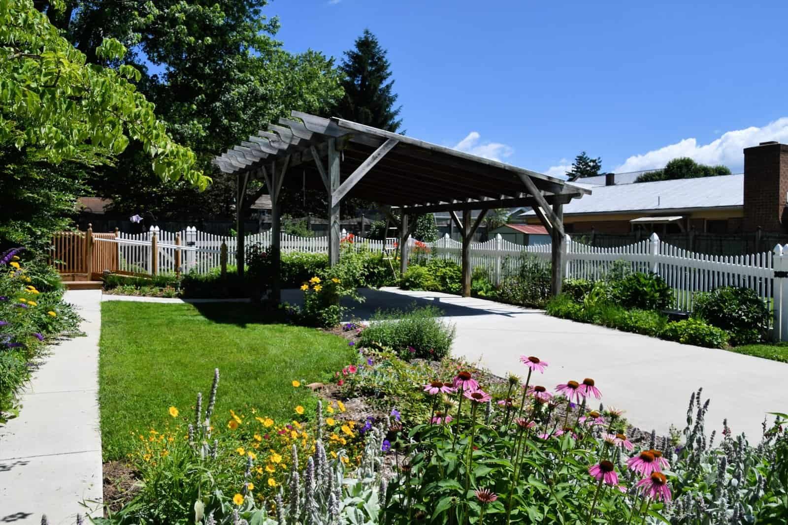 Garden shelter with wooden roof and surrounding colorful flowers and greenery.